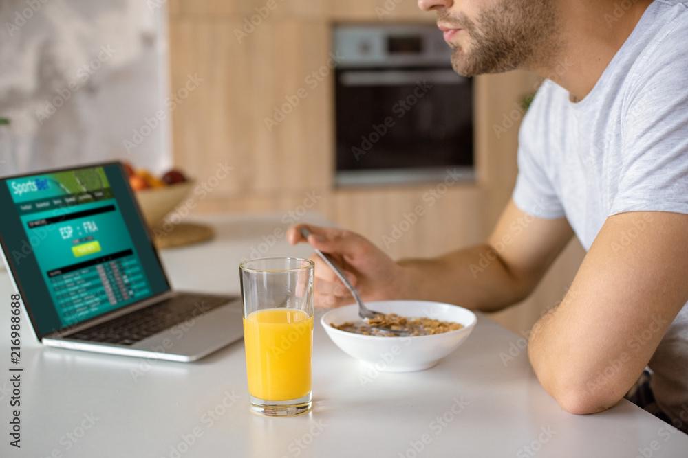 cropped image of man eating flakes with milk at kitchen table with fresh juice in glass and laptop with sportsbet on screen cropped image of man eating flakes with milk at kitchen table with fresh juice in glass and laptop with sportsbet on screen