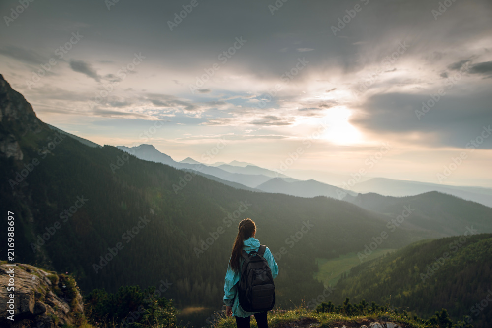 Rear shot of young packpacker woman standing on the mountain summit and enjoying beautiful sunset and Rysy mountains in Tatras, Poland, Slovakia