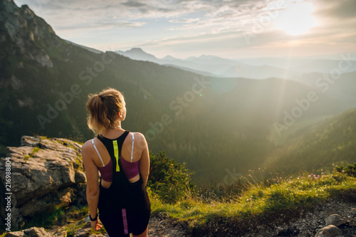 Rear view shot of young fit woman in sportswear looking on the scenic view of mountains on sunset. Rysy mountains, Tatras. Poland, Slovakia