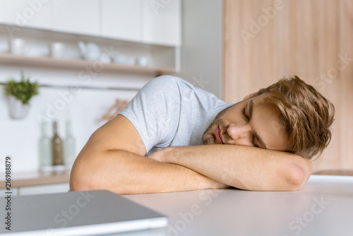 young man sleeping at kitchen table with laptop