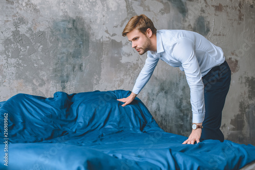 focused businessman covering bed by blue coverlet at home