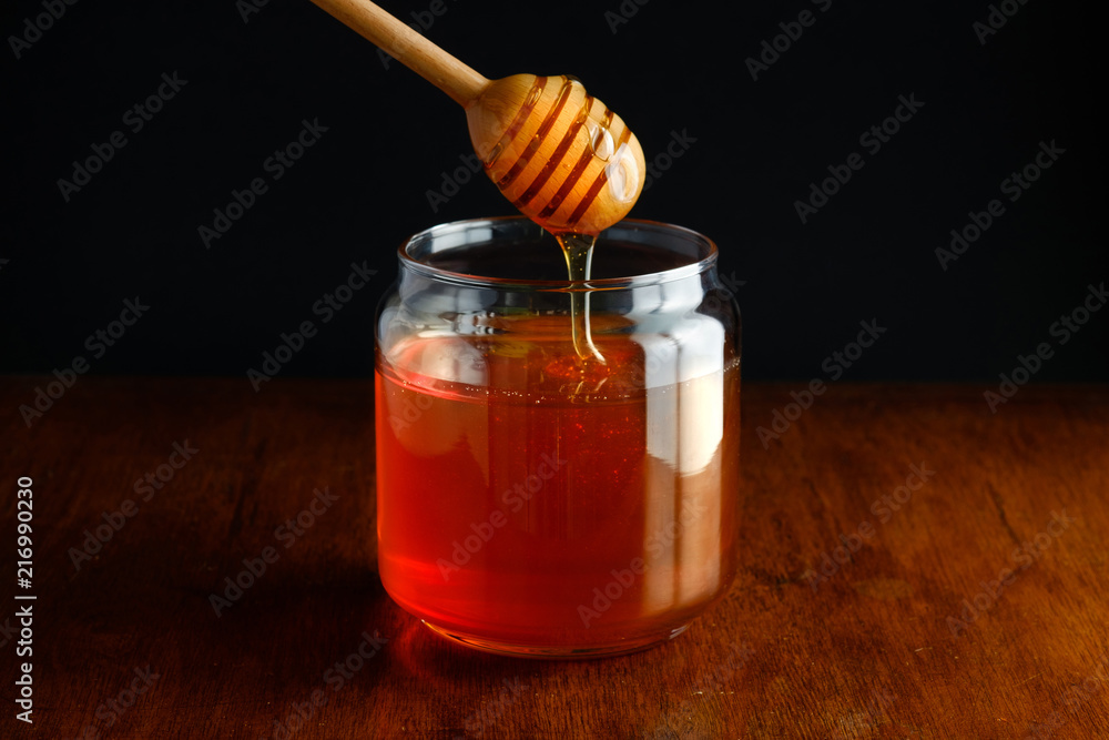 Jar of honey and a wooden dipper on wooden rustic table Jar of honey and a wooden dipper on wooden rustic table