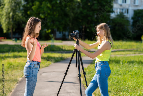 Where little teenage girls in the summer in park are recording video on the camera. Emotionally gesticulates with his hand using a camera with a tripod. photo