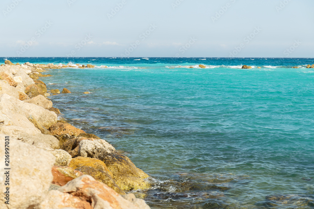Beautiful landscape of turquoise clear blue sea with rocks and breakwater and mountains in the background Beautiful landscape of turquoise clear blue sea with rocks and breakwater and mountains in the background