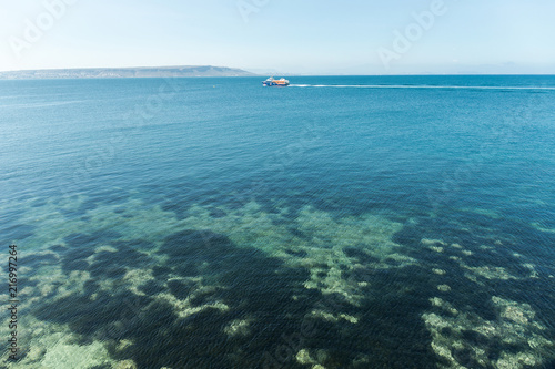 Clear and transparent water of the Mediterranean or Caribbean sea with boats and mountains in the background.
