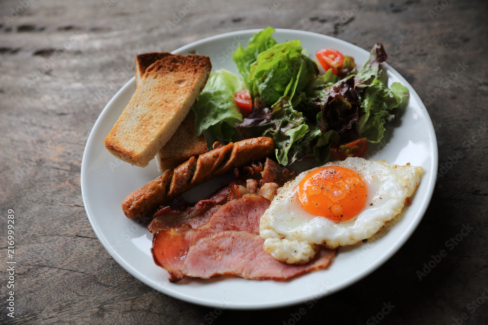 English breakfast fried egg, ham,sausage, bacon,salad and toast on wood background in mystic light English breakfast fried egg, ham,sausage, bacon,salad and toast on wood background in mystic light