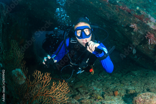 Female SCUBA diver in an underwater coral swimthrough on a dark tropical reef