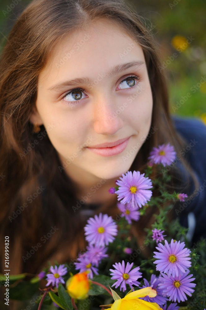 Teen girl sits next to flowers that bloom violet flowers and dreamingly looks up Teen girl sits next to flowers that bloom violet flowers and dreamingly looks up