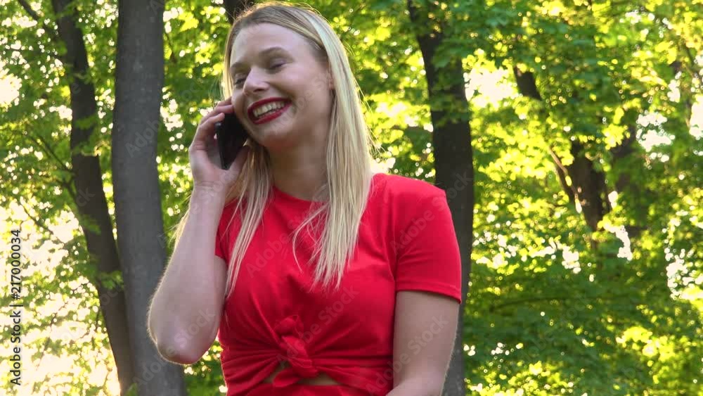 A young beautiful woman talks on a smartphone in a park on a sunny day - view from below A young beautiful woman talks on a smartphone in a park on a sunny day - view from below