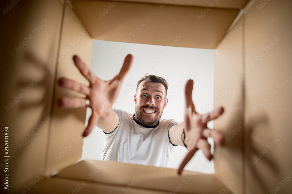 The surprised man unpacking, opening carton box and looking inside. The ...