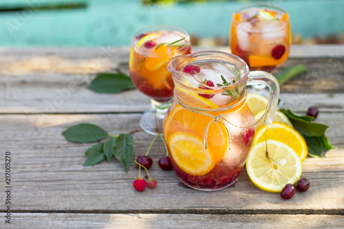 Homemade refreshing wine sangria or punch with fruits in glasses. Sangria cocktails with fresh fruits, berries and rosemary. On a wooden rustic table, with a jug and ingredients. Copy space.