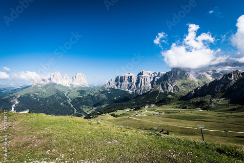 View of the valley dominated by Sass Pordoi immersed in the clouds and the Plattkofel and Langkofel illuminated in the blue sky