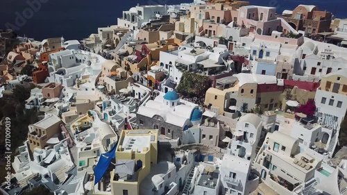 Aerial drone shot over white buildings in the hill with tourists shopping in the market in Oia, Santorini Greece