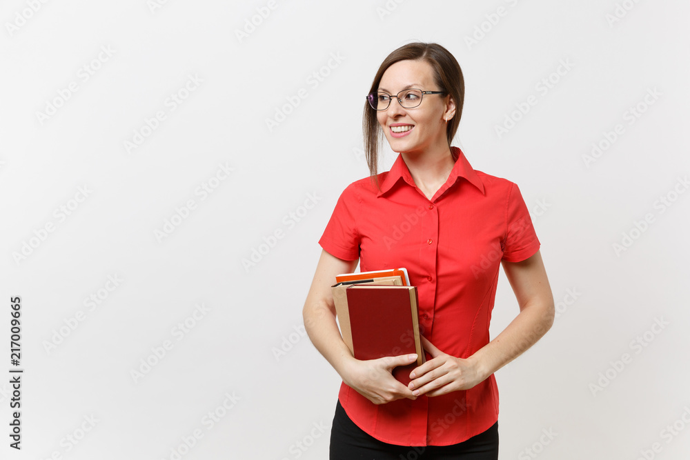 Portrait of young business teacher woman in red shirt, skirt and glasses looking aside, holding books in hands isolated on white background. Education or teaching in high school university concept. Portrait of young business teacher woman in red shirt, skirt and glasses looking aside, holding books in hands isolated on white background. Education or teaching in high school university concept.