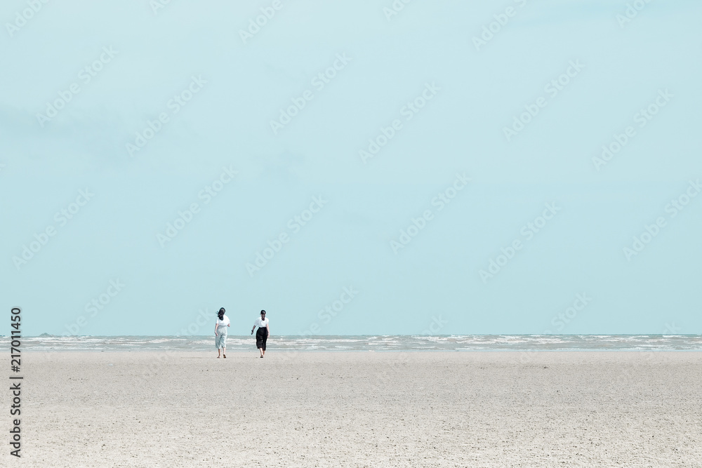 Two women walking on the beach to the calm sea