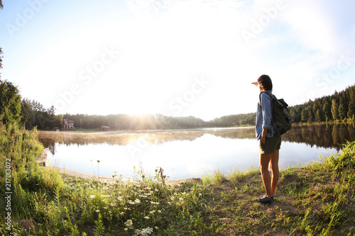 Young woman on shore of beautiful lake, wide-angle lens effect. Camping season