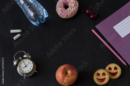 on a black background a notebook, an alarm clock and colored pencils, school supplies