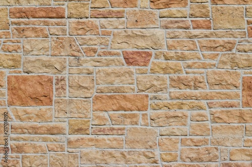 Aged fossiliferous limestone brick wall background in shades of orange, pink, yellow, and beige