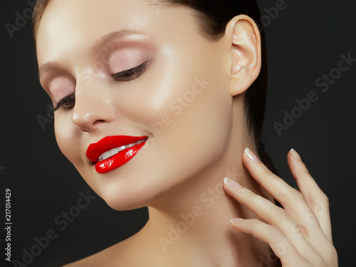 Gorgeous Young Brunette Woman face portrait. Beauty Model Girl with perfect eyebrows  clean make-up  red lips  touching her face. Sexy lady makeup for party. Isolated on black background
