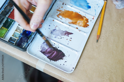 Artist paints with watercolor and kneads paints in a plastic palette.