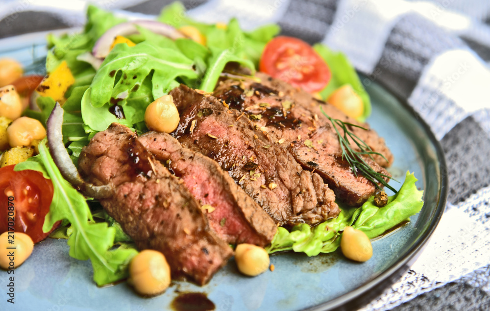 Steak Salad with Honey Soy Pan Sauce on blue dish..Beef salad with Arugula and chickpeas.