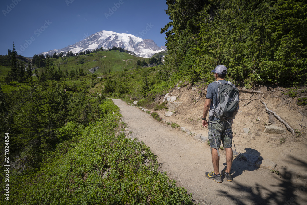 A young hispanic man is hiking on Mt.Rainier, Washington. The trail is pointing at the summit of Mt.Rainier.