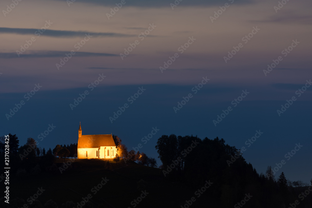 Beleuchtete Kirche auf Berg zur blauen Stunde