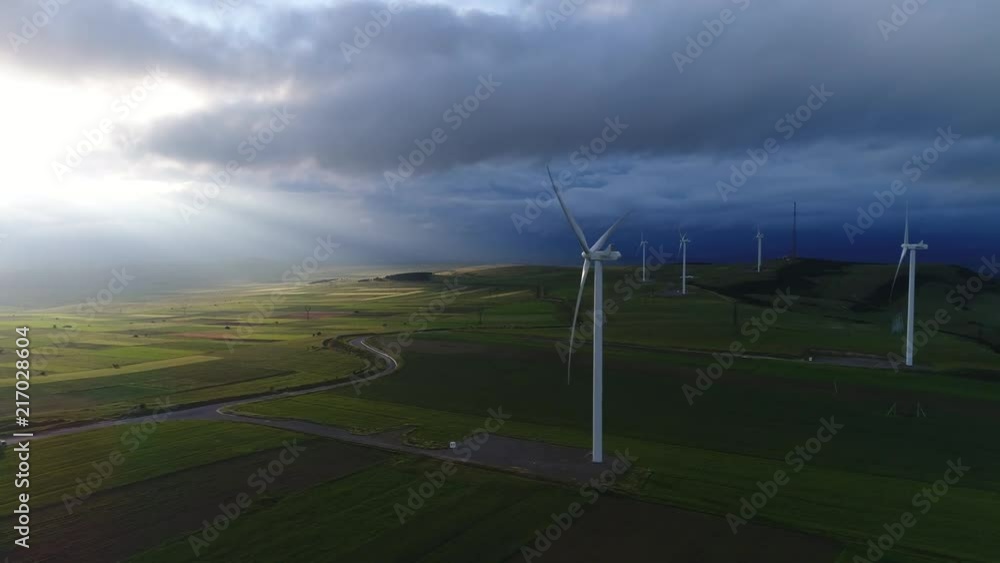 Aerial view. Wind turbines rotate among the fields and hills on the background of the picturesque evening sky. Natural production of pure energy from renewable ecologic sources. Aerial view. Wind turbines rotate among the fields and hills on the background of the picturesque evening sky. Natural production of pure energy from renewable ecologic sources.