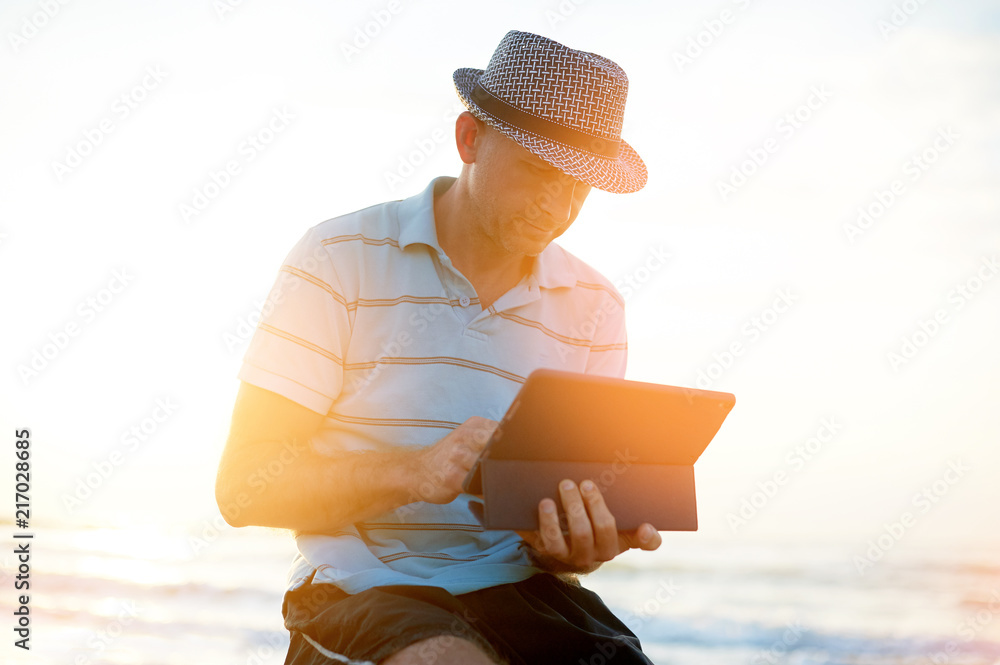 Senior man working on his laptop on the beach during sunset, freelancer concept in travel