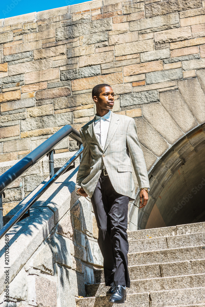 Young Happy African American Businessman traveling in New York City, wearing patterned blazer, white undershirt, black pants, leather shoes, walking down rock stairs by railing, looking around..