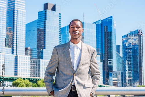 Young African American Businessman thinking outdoor in New York City, wearing patterned blazer, white shirt, standing in business district with high buildings under sun, narrowing eyes, sad, frowned..