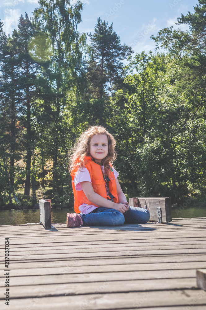 child in life jacket sitting on the pier.