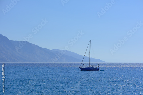 the sailing yacht floating in the sea against the background of the rocky mountain coast