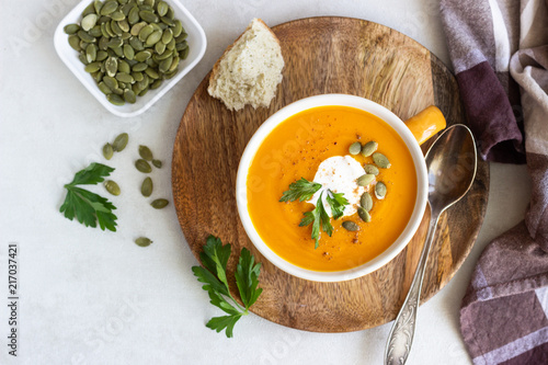 Roasted pumpkin soup with cream, parsley and pumpkin seeds on light background. 