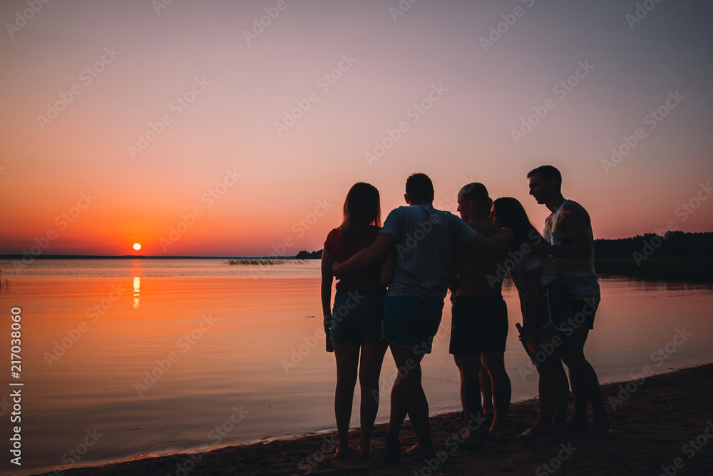 Holiday with friends in nature. Silhouette of friends at the beach looking on the sunset in the summer evening	