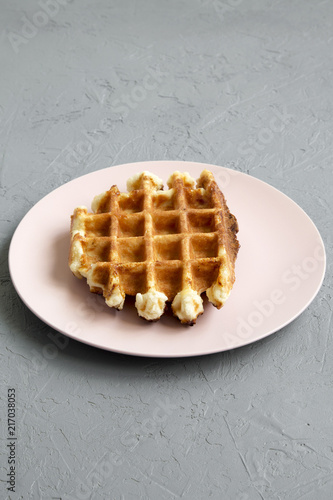 Traditional belgian waffle on pink plate over concrete background, side view.