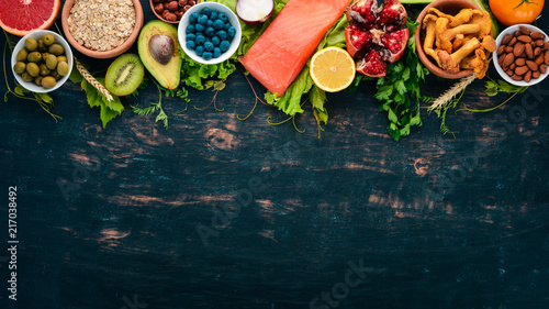A set of healthy food. Fish, nuts, protein, berries, vegetables and fruits. On a black wooden background. Top view. Free space for text.