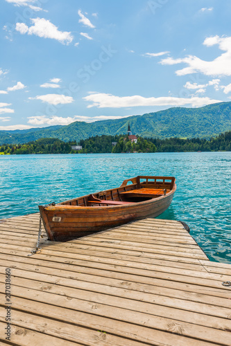 Harbor and boat on the Bled lake, Slovenia. Wooden boats on the pure blue water. Summer day near the Alps and forest © Martin