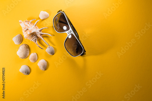 Sunglasses with shell on yellow background. Summer concept