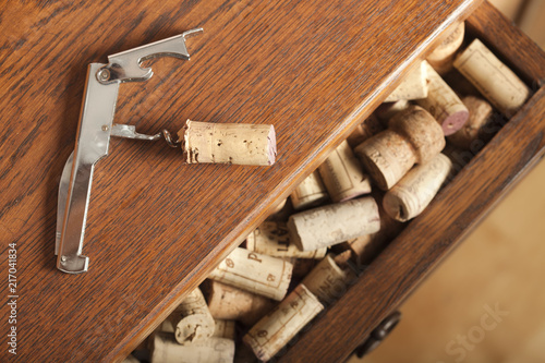 Cork on corkscrew placed on wooden sideboard with open drawer full of corks. Focus on the corksrew and cork. photo