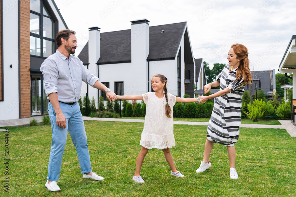 Obraz premium Carefree childhood. Joyful nice girl smiling while standing together with her parents