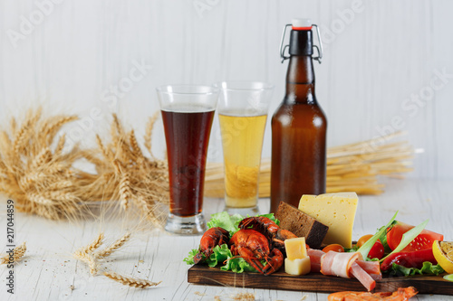 snack with cancer, cheese, tomato, ham, lemon and beer on white table, on white background. Two glasses of gold and dark beer and a bottle of beer