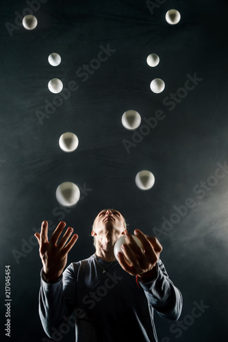 Cuadro en lienzo Blond juggler with white balls on black background