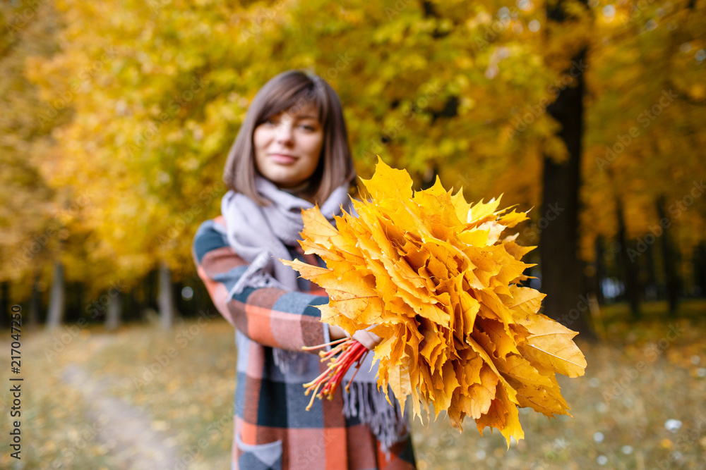 Focus on yellow leaves. Brunette woman in autumn park with fashionable plaid coat and scarf. Focus on yellow leaves. Brunette woman in autumn park with fashionable plaid coat and scarf.