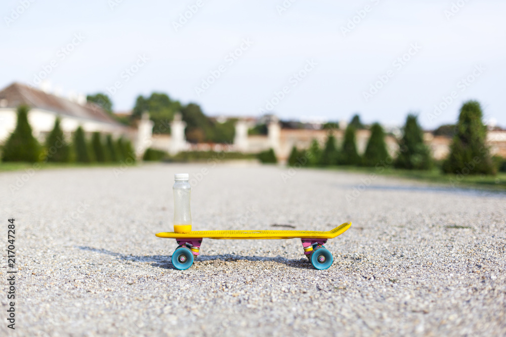 Obraz premium Gesundes Getränk auf gelben Skateboard im Park. Healthy drink standing on a yellow skateboard in a park.