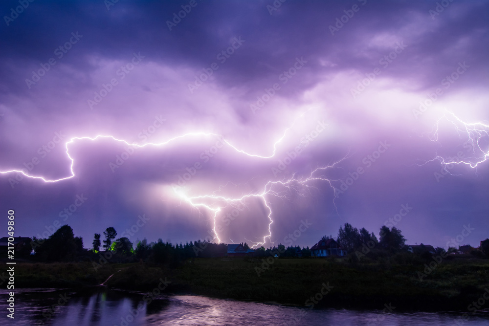 Composition photo of different lightning bolts. Thunderstorm with dramatic clouds. Lots of lightnings over the night village near river bank. Bad weather concept. Composition photo of different lightning bolts. Thunderstorm with dramatic clouds. Lots of lightnings over the night village near river bank. Bad weather concept.