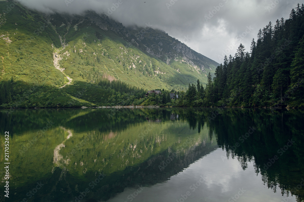 Fototapeta premium Foggy green mountain forrest and hills with a reflection on the lake, morskie Oko in High Tatras, Zakopane, Poland