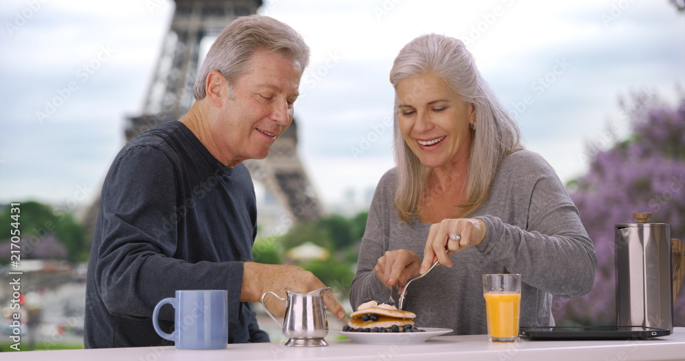 Older white male and female near Eiffel Tower eat delicious breakfast pastry Older white male and female near Eiffel Tower eat delicious breakfast pastry