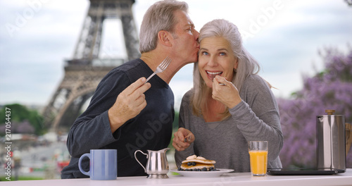 Older white male and female near Eiffel Tower eat delicious breakfast pastry