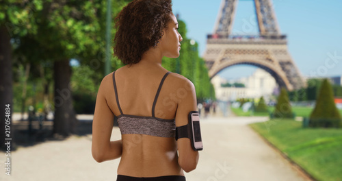 Photography Pretty African female in sports clothes stands near Eiffel Tower looking around